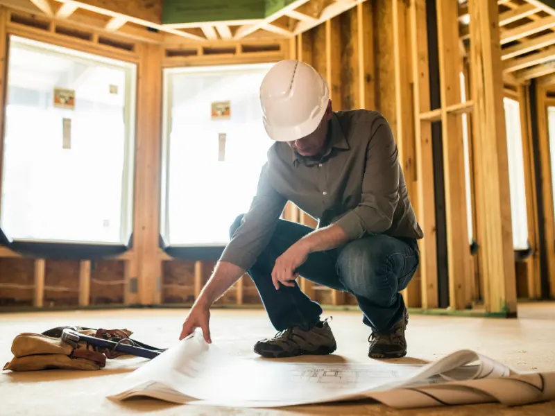 contractors internet marketing Construction worker reviewing building plans indoors.